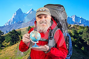 bearded tourist in a red jacket holds a model of the world globe in his hands. tourism and travel around the world