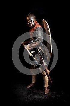 Bearded warrior in the armor  of the Viking Age holds a lance and sword