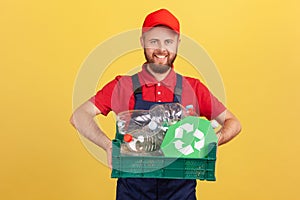 Bearded worker man standing and holding box with plastic bottles and recycling sign.