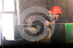bearded worker in protective helmet repairing machine tool