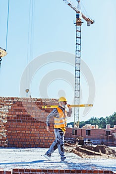 Bearded worker in reflective vest and hardhat walking with spirit level across