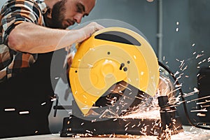 Bearded worker using electrical grinding machine in service station. Work in action. Sparks fly apart