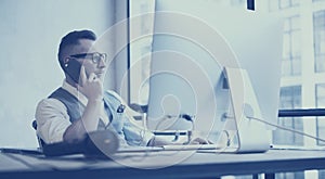 Bearded young businessman wearing white shirt,waistcoat and working at the desktop computer in modern loft.Stylish man