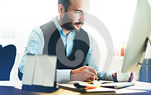 Bearded young businessman working on modern office. Consultant man thinking looking in monitor computer. Manager typing on keyboar photo