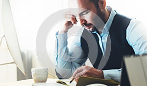 Bearded young businessman working on modern office. Consultant man thinking looking in monitor computer. Manager writes in noteboo photo