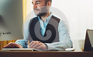 Bearded young businessman working on modern office at night. Consultant man thinking looking in monitor computer. Manager typing o photo