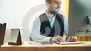 Bearded young businessman working on modern office at night. Consultant man thinking looking in monitor computer. Manager typing o photo