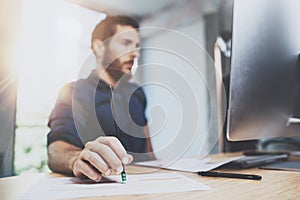 Bearded young coworker working at sunny office. Man using contemporary desktop computer and making notes in notebook