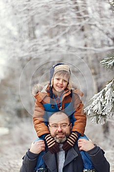Bearded young father and l little son on walk in winter forest. Boy sits in man shoulders. Christmas vacation