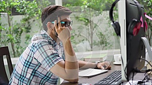 Bearded young  Freelancer man thinking and take a note on dask with computer working at home