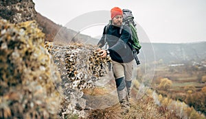 Bearded young male hiking in mountains with travel backpack. Traveler man trekking during his journey