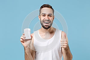 Bearded young man 20s years old in white shirt hold using antiperspirant isolated on blue pastel wall background, studio