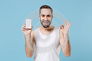 Bearded young man 20s years old in white shirt hold using antiperspirant isolated on blue pastel wall background, studio