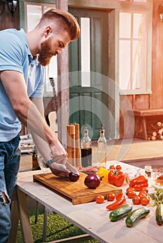 Bearded young man cutting onion for barbecue