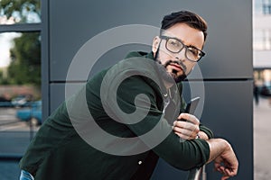Bearded young man in eyeglasses holding smartphone