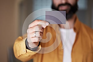 Bearded young man giving hand empty black business card on blurred background. Mockup Copy Paste Blank Advertisement.
