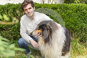 Bearded young man kneeling with hairy collie dog outdoors