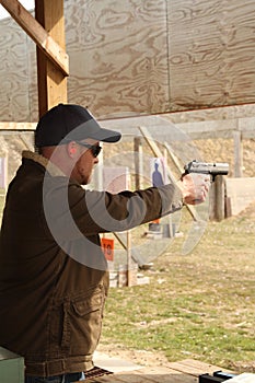Bearded young man shooting handgun at pistol range targets