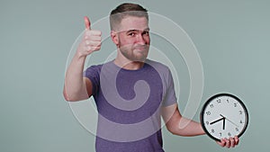 Bearded young man showing time on clock watch, ok, thumb up, approve, pointing finger at camera