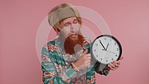 Bearded young man showing time on clock watch, ok, thumb up, approve, pointing finger at camera