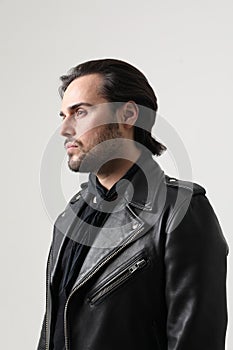 Bearded young man wearing black biker jacket posing indoor. Vertical mock-up.