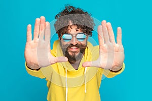 Bearded young man in yellow hoodie holding palms up and framing