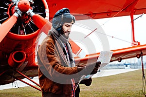 A bearded young pilot, a traveler stands on the background of a red old-fashioned airplane and studies the map