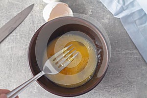 Beat an egg with a fork in a brown clay plate on the table