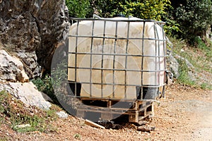 Beaten down old heavily used intermediate bulk container or IBC plastic tank with twisted metal cage put on wooden pallets