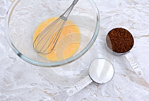 Beaten egg with whisk and measuring cups of sugar
