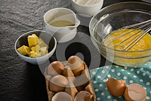 Beaten eggs, egg tray, butter, oil and flour kept on a black surface