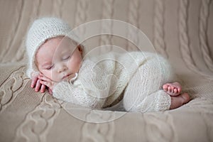 Beatiful baby boy in white knitted cloths and hat, sleeping