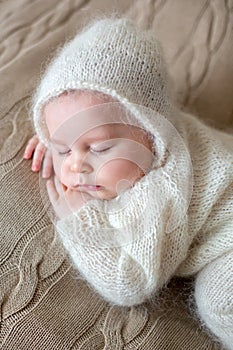 Beatiful baby boy in white knitted cloths and hat, sleeping