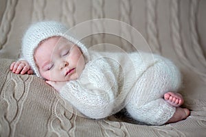 Beatiful baby boy in white knitted cloths and hat, sleeping