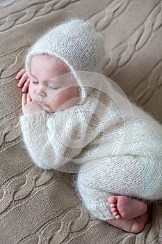 Beatiful baby boy in white knitted cloths and hat, sleeping