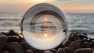 Beatiful background landscape inside crystal ball lay on beach stones, sunset and ocean waves inside