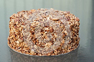 Nut biscuit cake finished with crushed sugar-coated candied caramelized almonds on a glass table