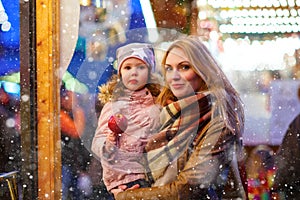 Beatiful woman and little kid girl eating crystallized sugared apple on German Christmas market. Happy family, mother