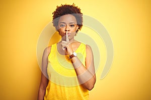 Beauitul african american woman wearing summer t-shirt over isolated yellow background asking to be quiet with finger on lips