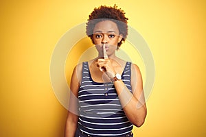 Beauitul african american woman wearing summer t-shirt over isolated yellow background asking to be quiet with finger on lips