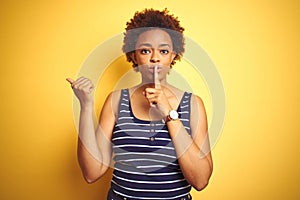 Beauitul african american woman wearing summer t-shirt over isolated yellow background asking to be quiet with finger on lips