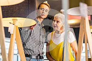 Beauteous aged madam and attractive mature man considering buying standard-lamps