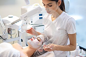 Beautician aplying face peeling mask, spa beauty treatment. Woman getting facial care by beautician at spa salon