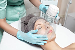Beautician applies face cream on beautiful young woman in Spa salon. cosmetic procedure skin care.