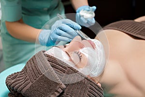 Beautician applies face mask on beautiful young woman in Spa salon. cosmetic procedure skin care. Microdermabrasion