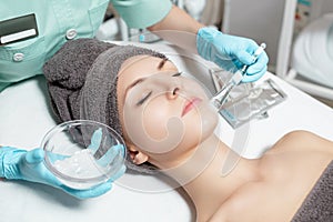 Beautician applies face mask with brush to beautiful young woman in Spa salon. cosmetic procedure skin care.