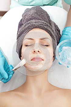 Beautician applies face mask with brush to beautiful young woman in Spa salon. cosmetic procedure skin care.