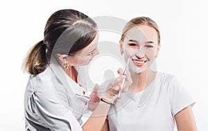 Beautician applies a mask on the face of a young beautiful girl, on a white background