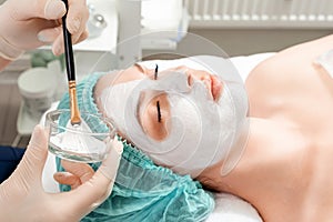 A beautician applies a mask to the face in a beauty salon. The concept of facial hygiene, cosmetic procedures, skin care, skin