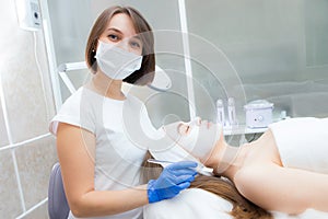 Beautician applies a natural moisturizing mask to the face of a young beautiful client